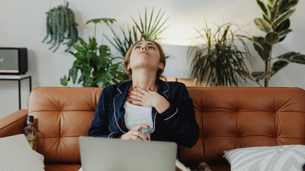 A woman sitting on a couch looking stressed with a hand on her chest.