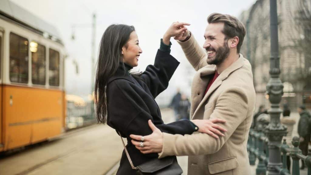 A couple smiling and dancing together near a tram.