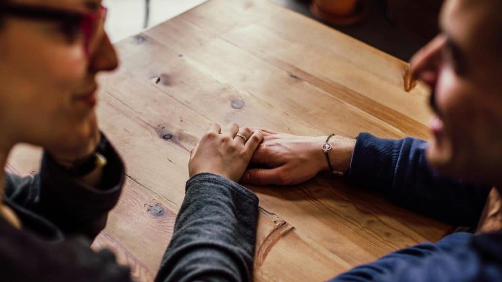 A couple holding hands across a wooden table.