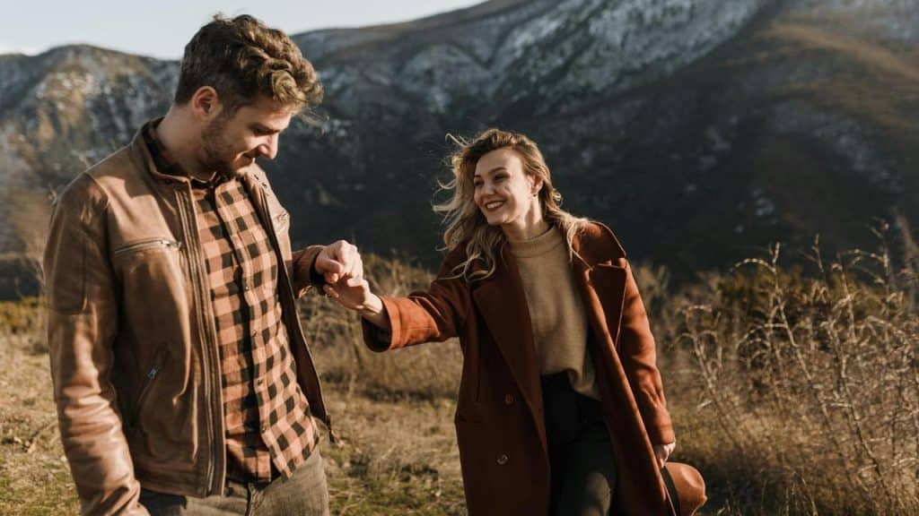 A couple walking outdoors while holding hands in a mountainous area.