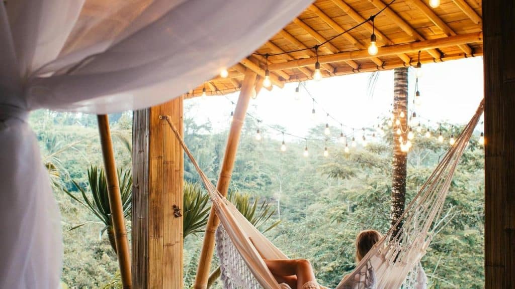 A person relaxing on a hammock under string lights in a tropical setting.