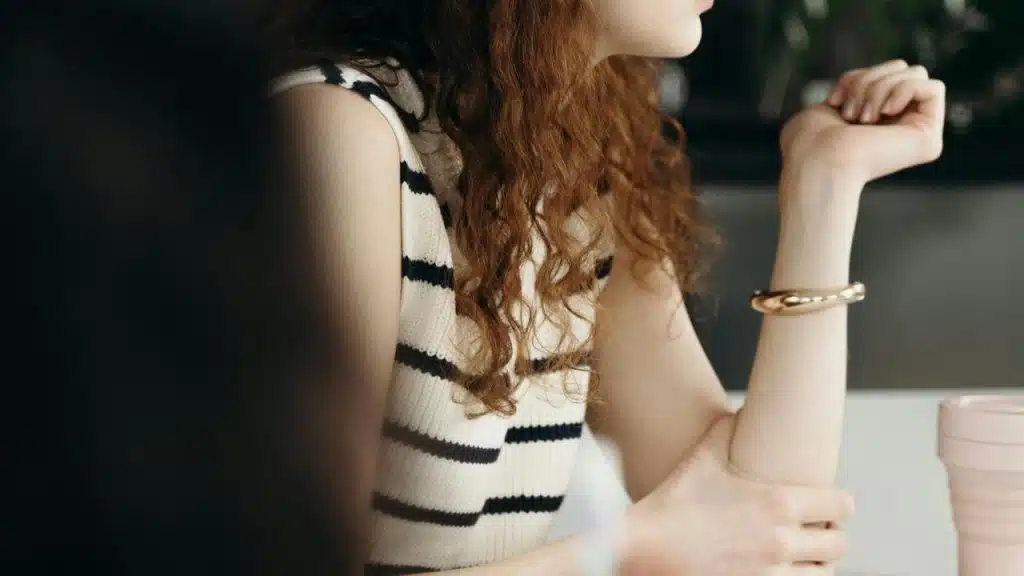 A person with curly hair wearing a striped sleeveless top sitting at a table.