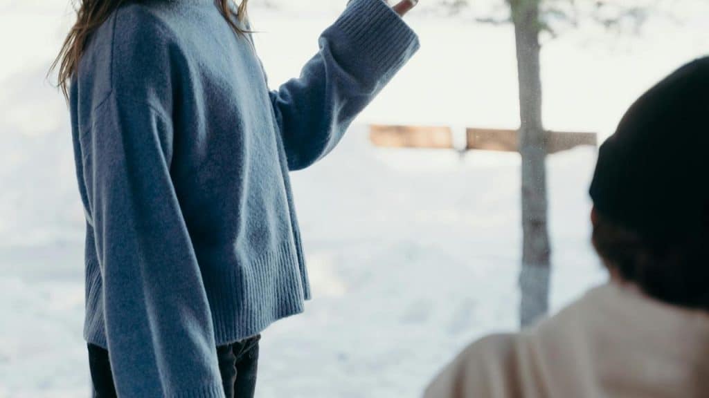 A person in a blue sweater standing and gesturing while another person sits nearby.
