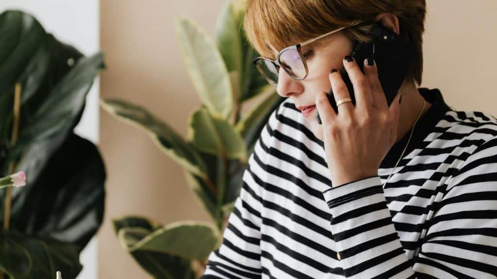 A woman wearing glasses and a striped shirt talking on the phone indoors.