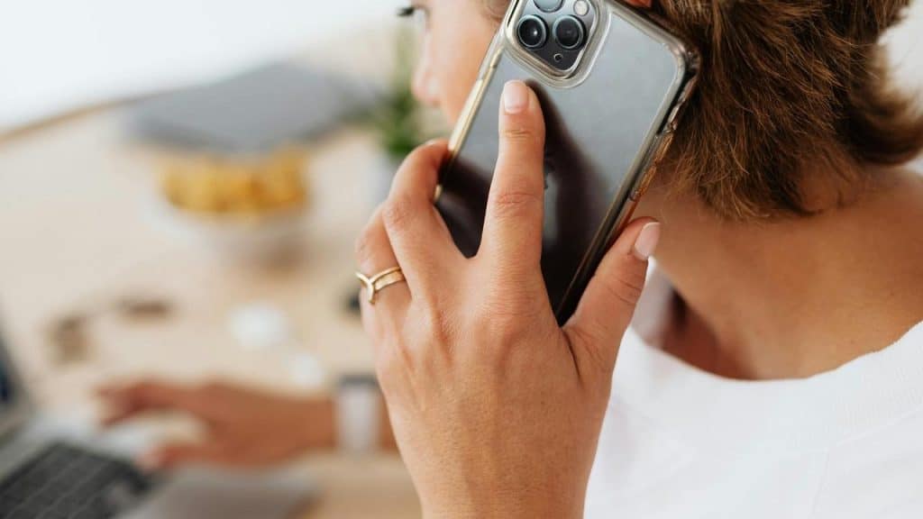 A woman holding a smartphone to her ear while working on a laptop.