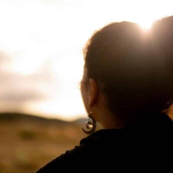 An image of a person with their hair in a bun looking toward the sunset.