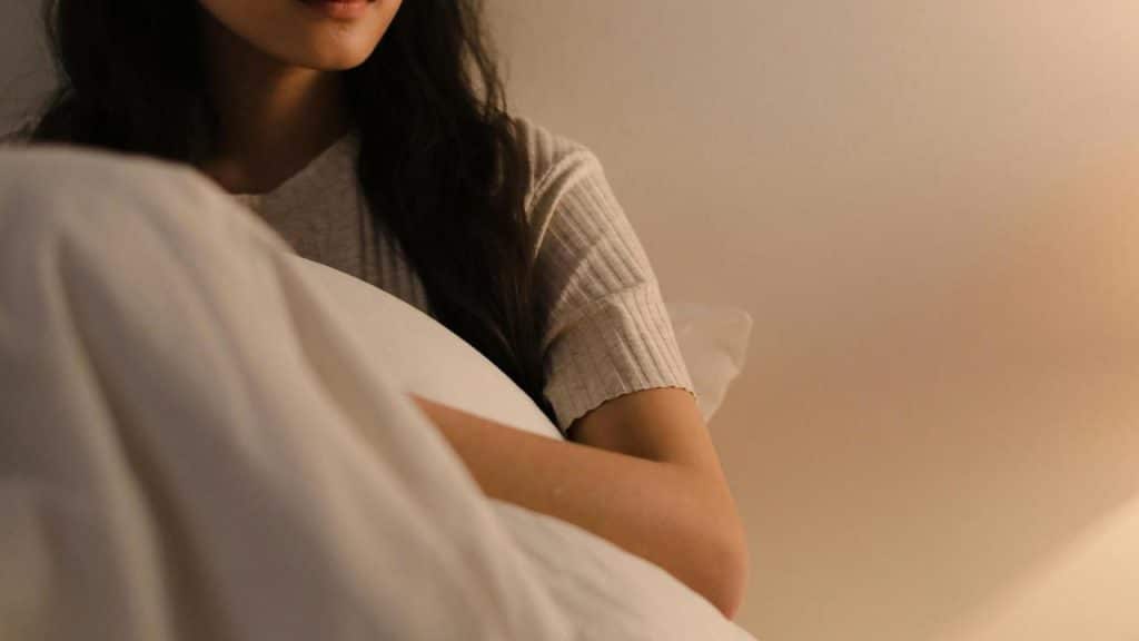 A woman sitting on a bed holding a pillow in a softly lit room.