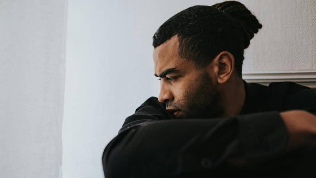 A man sitting indoors with his arms crossed, looking out thoughtfully.