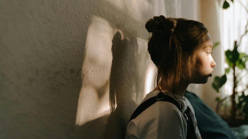 A girl sitting against a wall with sunlight casting her shadow.