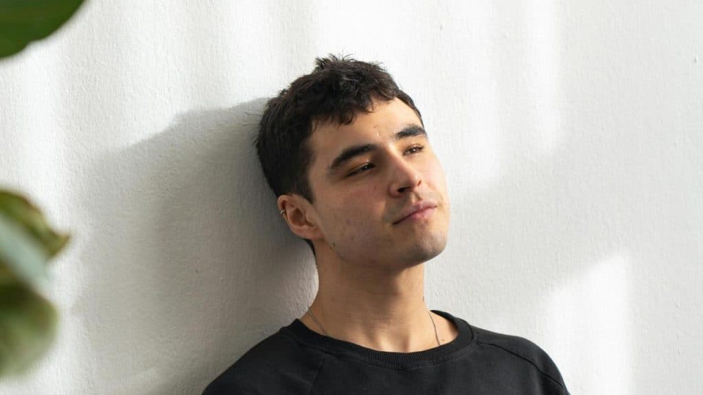 A man leaning against a wall looking thoughtful in natural light.