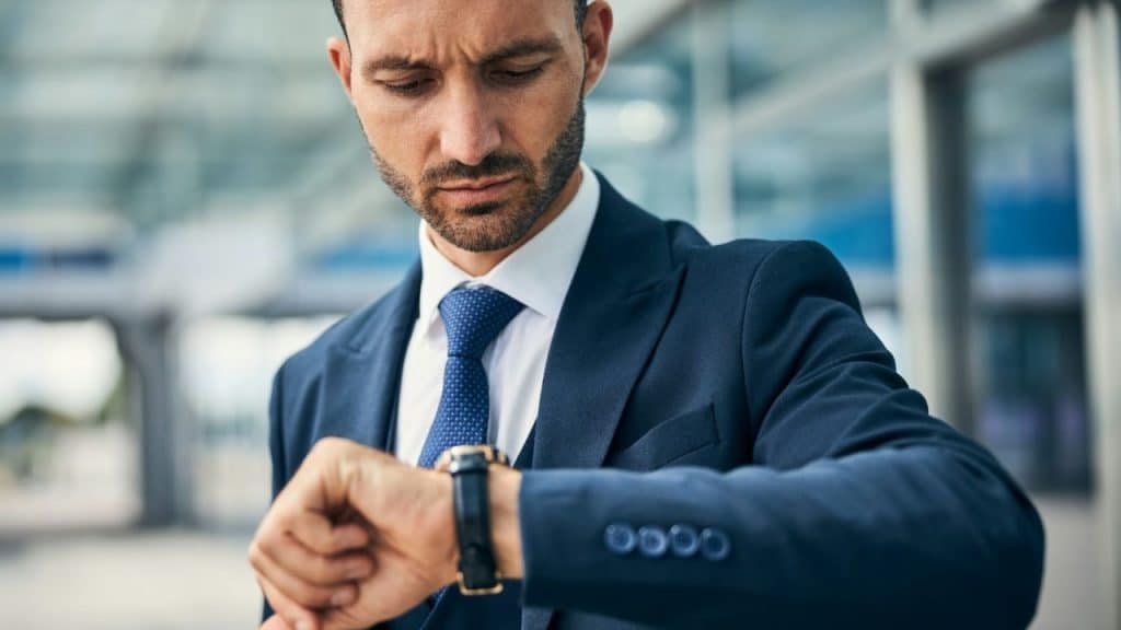 A sharply dressed businessman looking intently at his wristwatch outdoors.