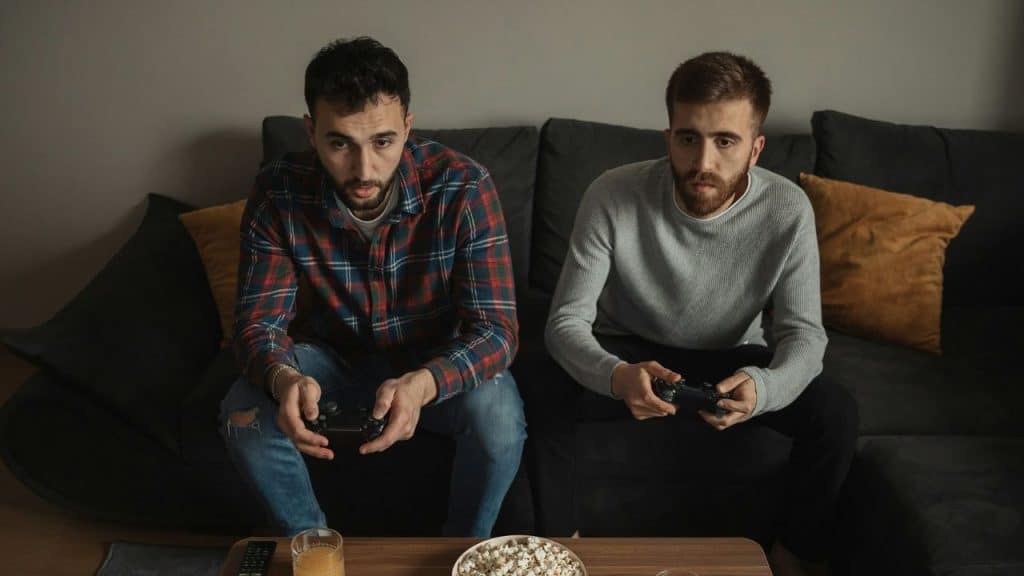Two intense young men on a couch playing a video game with controllers.