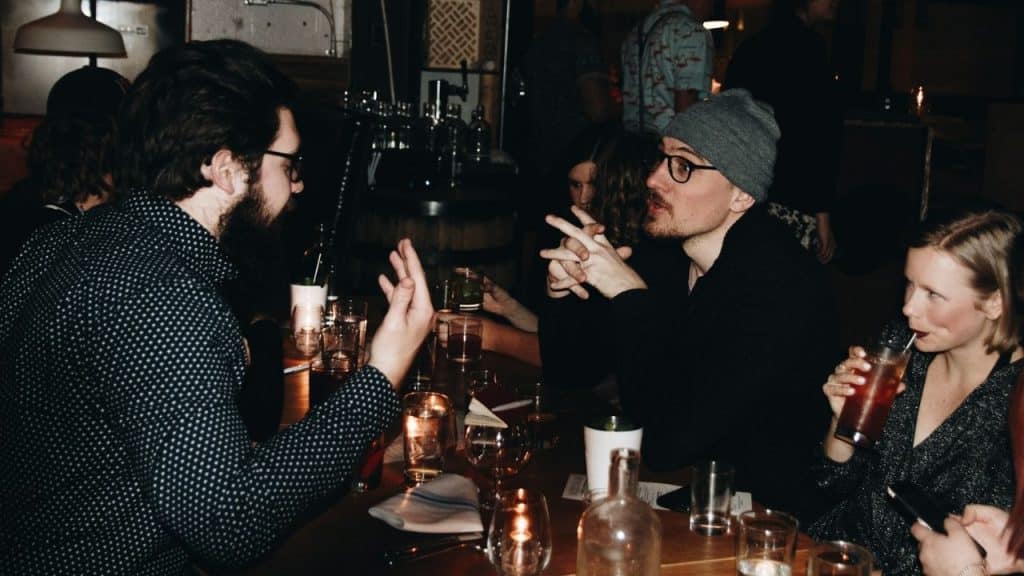 A dimly lit group of friends having a lively conversation at a dinner table.