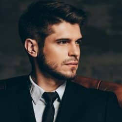 Young man in a black suit and tie sitting in a leather chair.