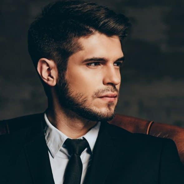 Young man in a black suit and tie sitting in a leather chair.