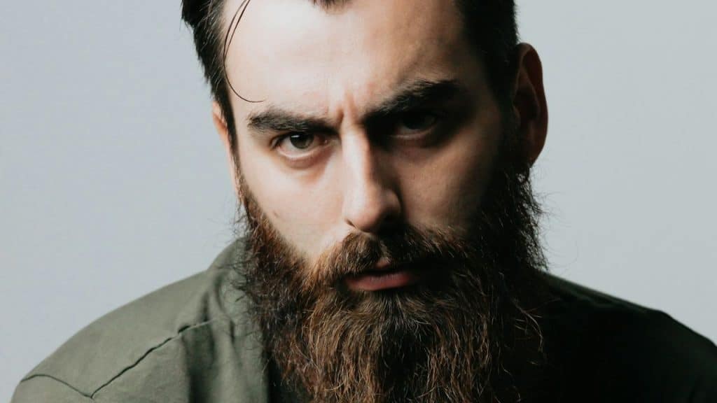 Close-up of a serious man with a long, thick beard and dark hair.