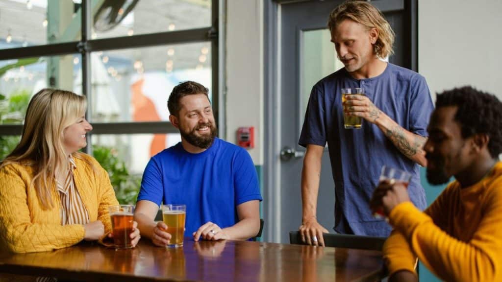 Four diverse people sitting and standing around a table with drinks in a casual setting.