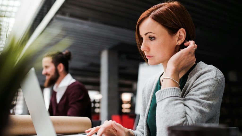 A focused woman with short red hair working on a laptop in a modern office space.