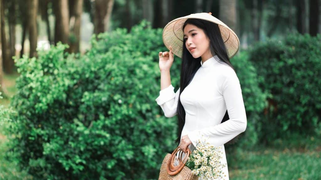 A woman in a white dress holding a straw hat.