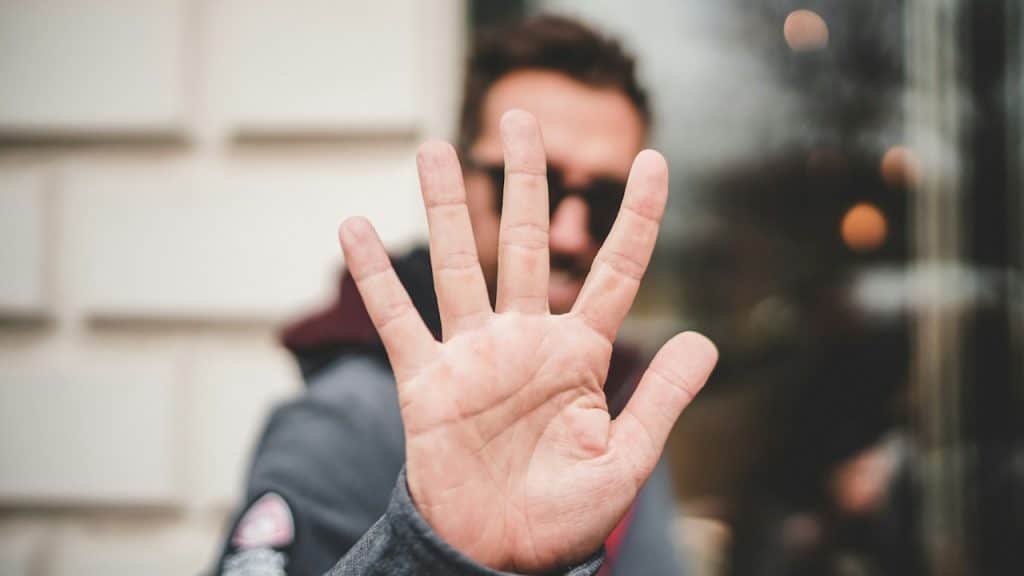 A man wearing glasses saying no with his hand held with palm outwards towards the camera.
