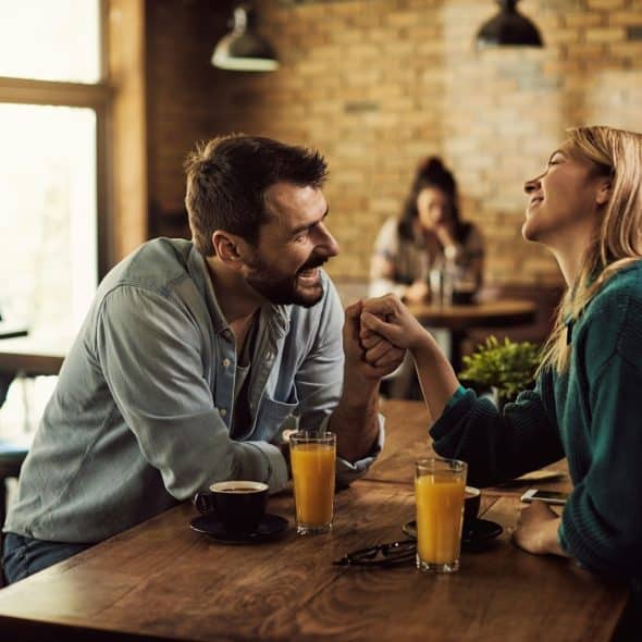 The man is holding the woman’s hand while having drinks in a café.