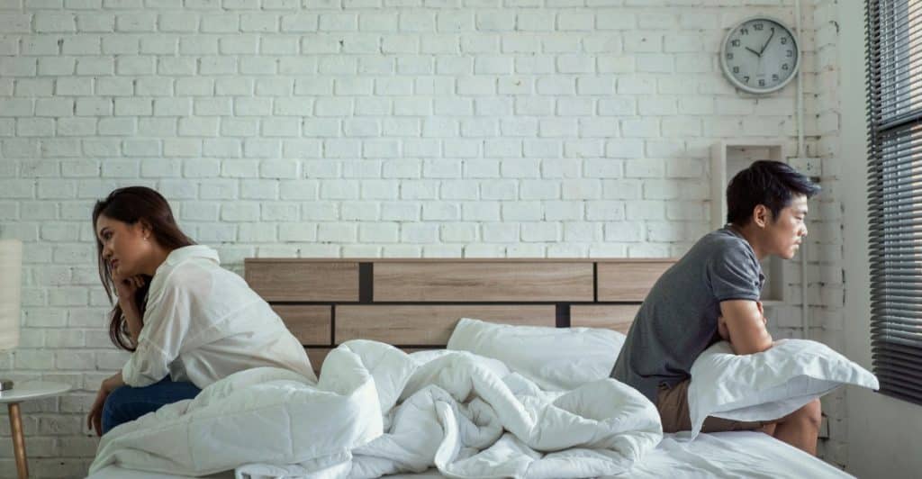 A man and woman sitting at the opposite end of bed