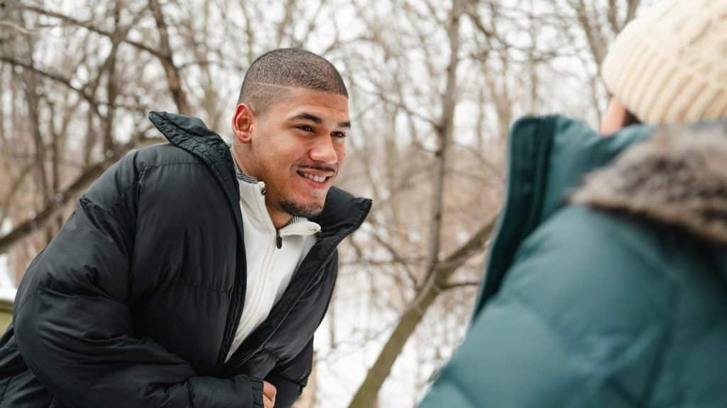 A man wearing a jacket is smiling and looking at a woman.