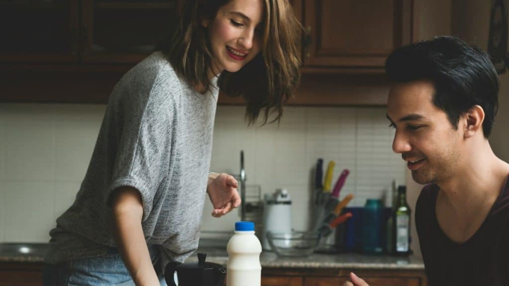 Woman and man standing together in a kitchen with a bottle of milk on the counter.