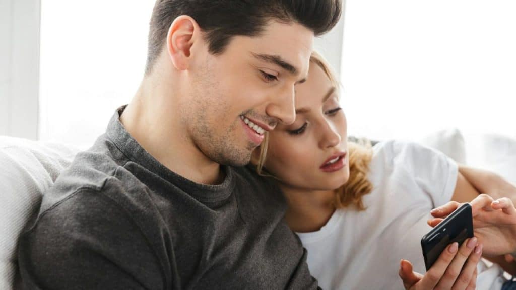 Man in a dark shirt and woman in a white shirt looking closely at a smartphone screen together.