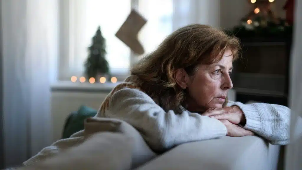 Mature woman resting on a couch, looking away thoughtfully near a window.