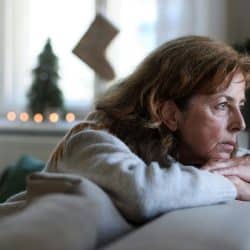 Mature woman resting on a couch, looking away thoughtfully near a window.