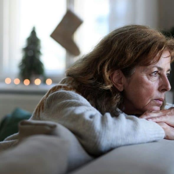 Mature woman resting on a couch, looking away thoughtfully near a window.
