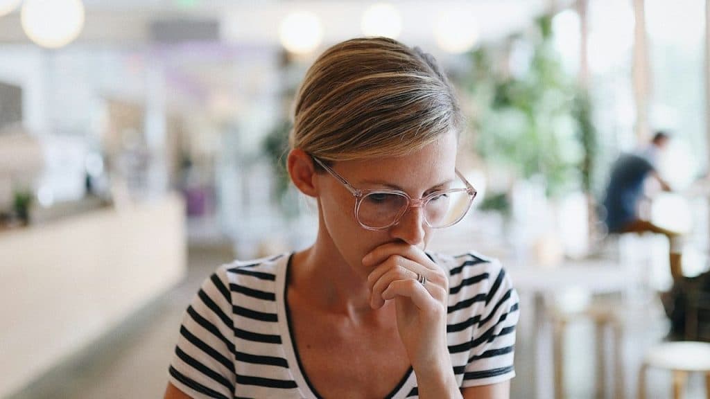 Woman in a striped shirt and glasses looking down, covering her mouth with her hand.