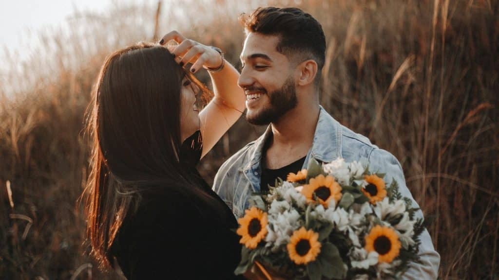 A cheerful man giving a bunch of yellow and white flowers to his girlfriend.
