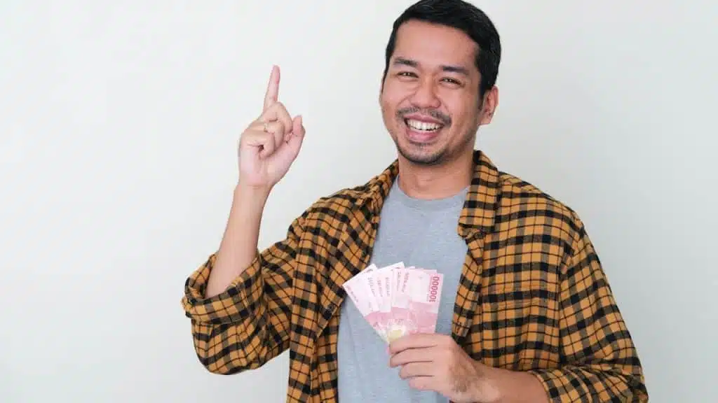 A man holding a bunch of cash in one hand and making a peace sign.