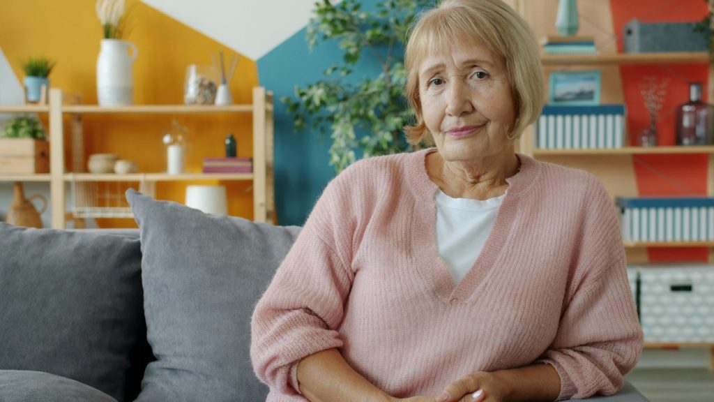 An elderly woman sitting on a couch in a colorful room.