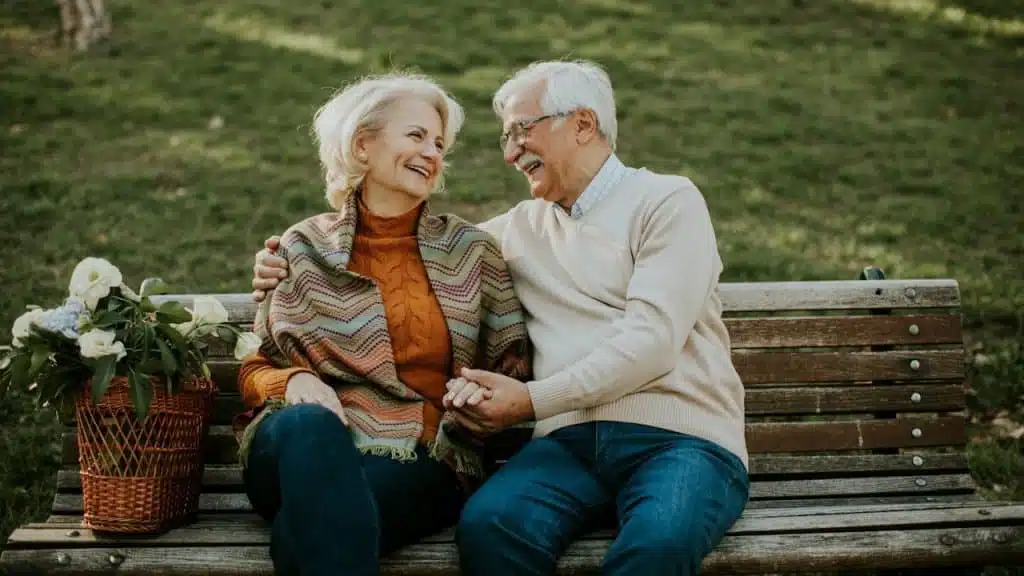An older couple sitting on a bench and smiling together.