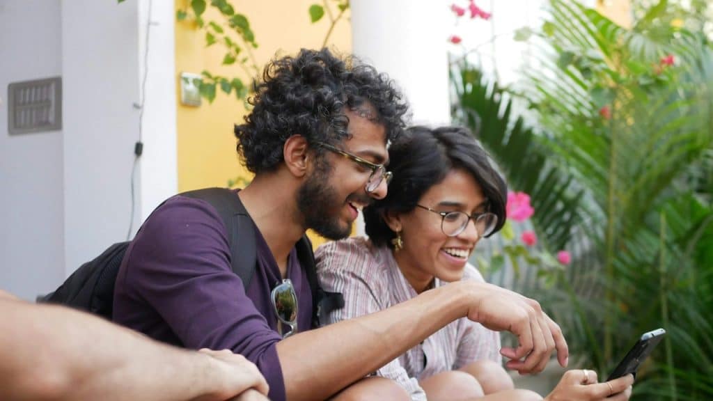 A man wearing glasses looking at a phone held by a woman wearing glasses. 