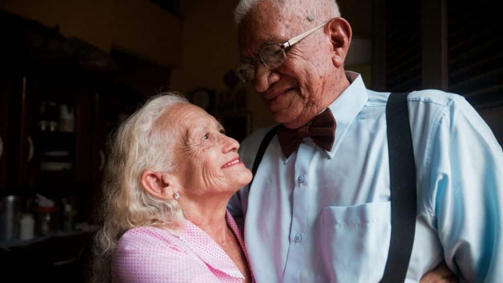 Elderly couple smiling at each other; the man wears a bowtie and glasses.