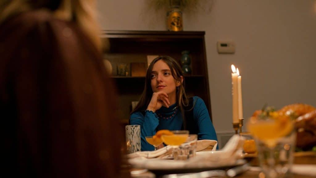 Woman at a dinner table looking away with her chin resting on her hand by candlelight.