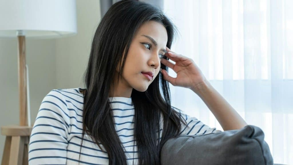 Young woman with long dark hair, wearing a striped shirt, looking away thoughtfully indoors.