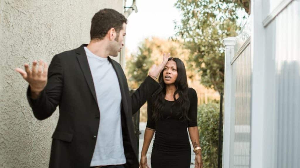 A man in a black jacket gestures at a woman in a black dress who is also gesturing.
