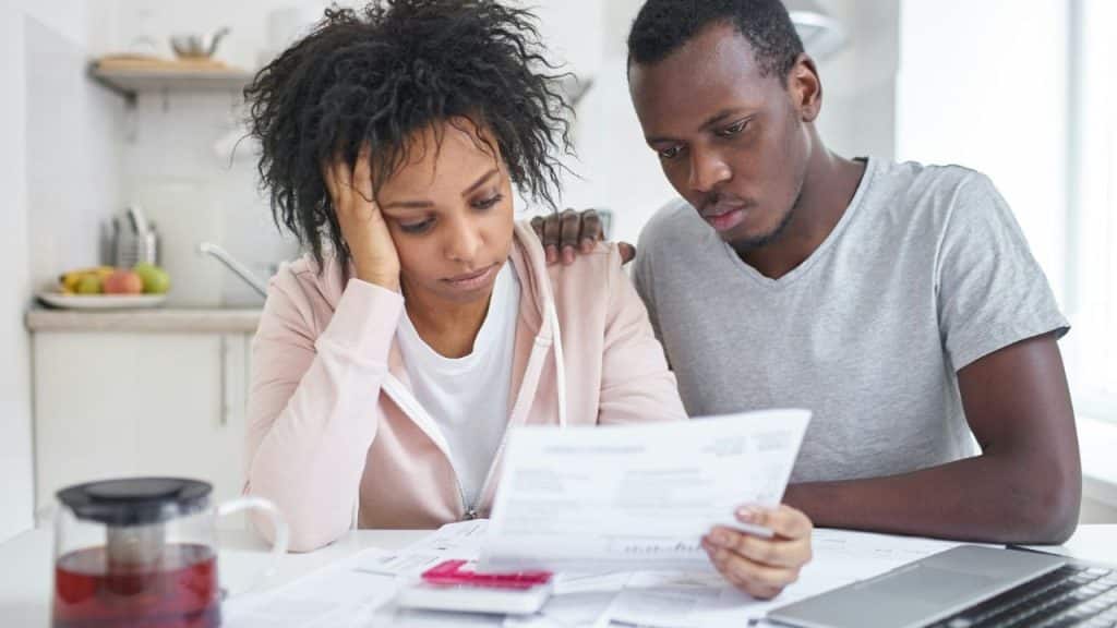 A distressed woman and a man look at papers on a kitchen table.