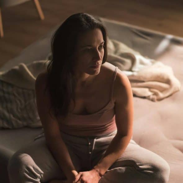 A woman sitting on the edge of a bed in soft, dim morning light.