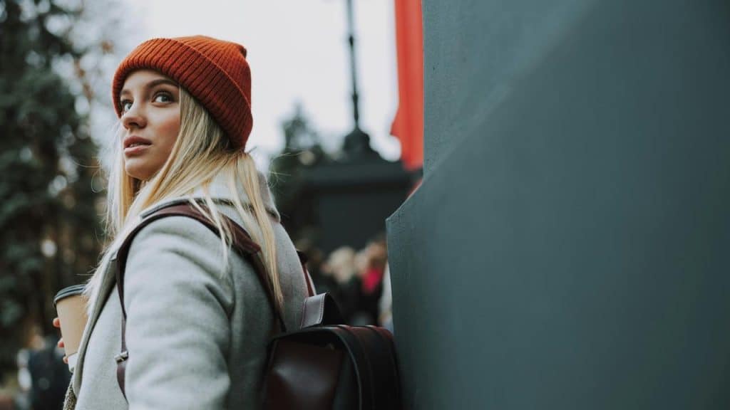 A woman in a red beanie looking back while holding a coffee cup outdoors.