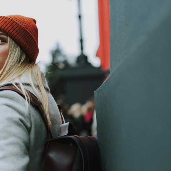 A woman in a red beanie looking back while holding a coffee cup outdoors.