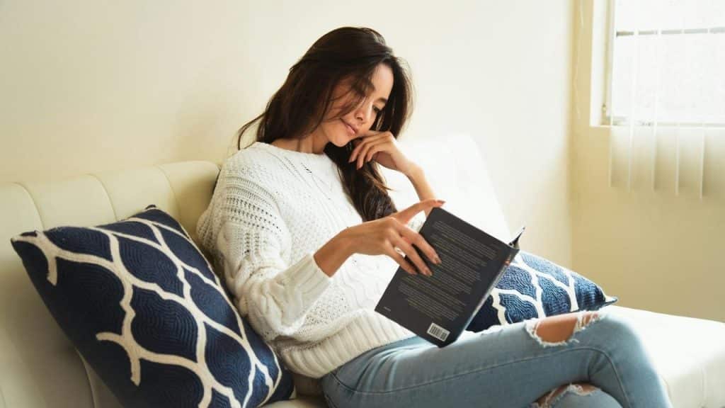 A woman sitting on a couch reading a book.