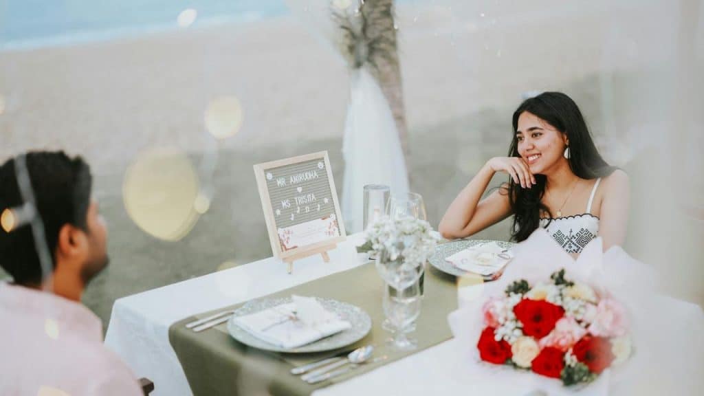 A smiling woman enjoys a beachside dinner with a man at a decorated table.