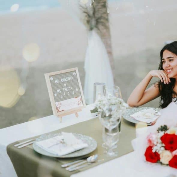 A smiling woman enjoys a beachside dinner with a man at a decorated table.