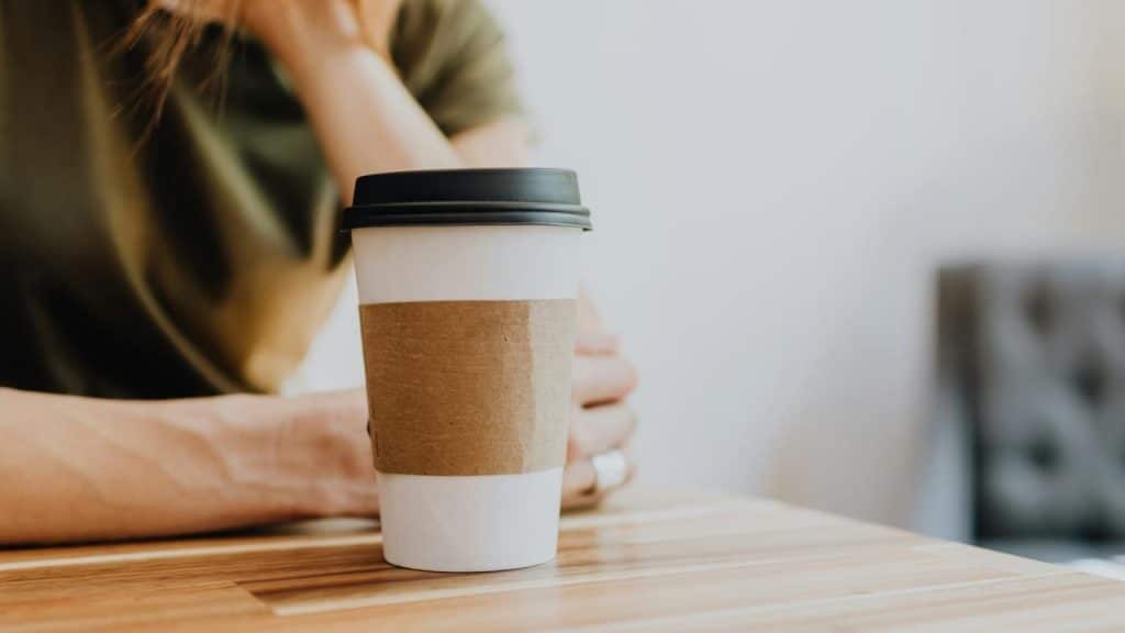A person with a disposable coffee cup sitting on a wooden table.